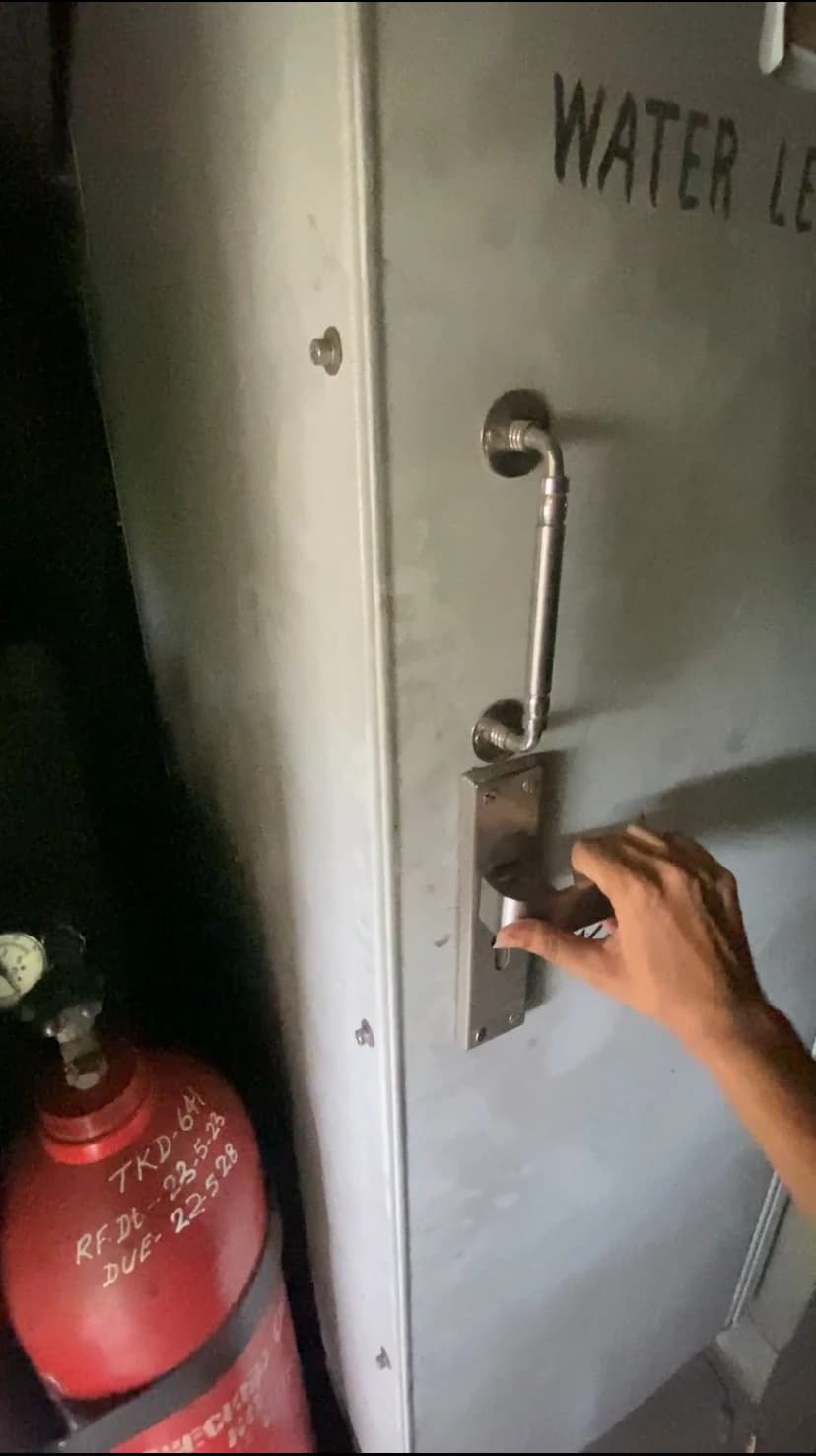 A hand reaching for the lavatory door's lock, a fire extinguisher crowding the doorway